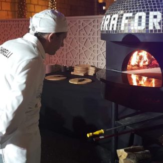 Chef in Dubai dressed in white checks on wood flame in brick oven