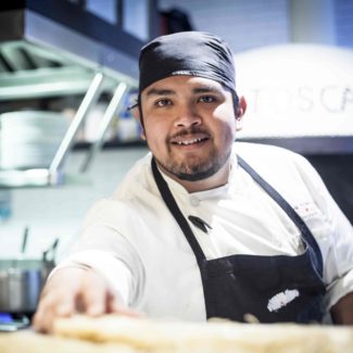Mexican Chef in pizza cafe toscano serves pizza