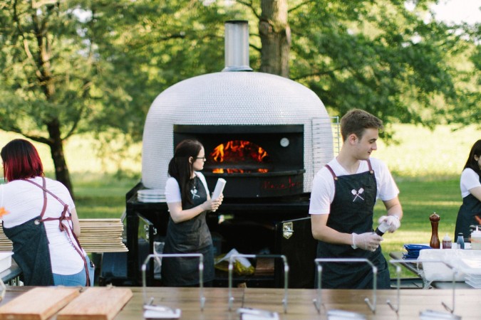 an image of wooden paddle restaurant based in Chicago, Illinois using marra forni's outdoor commercial mobile brick oven. The oven has flame inside from burning wood.